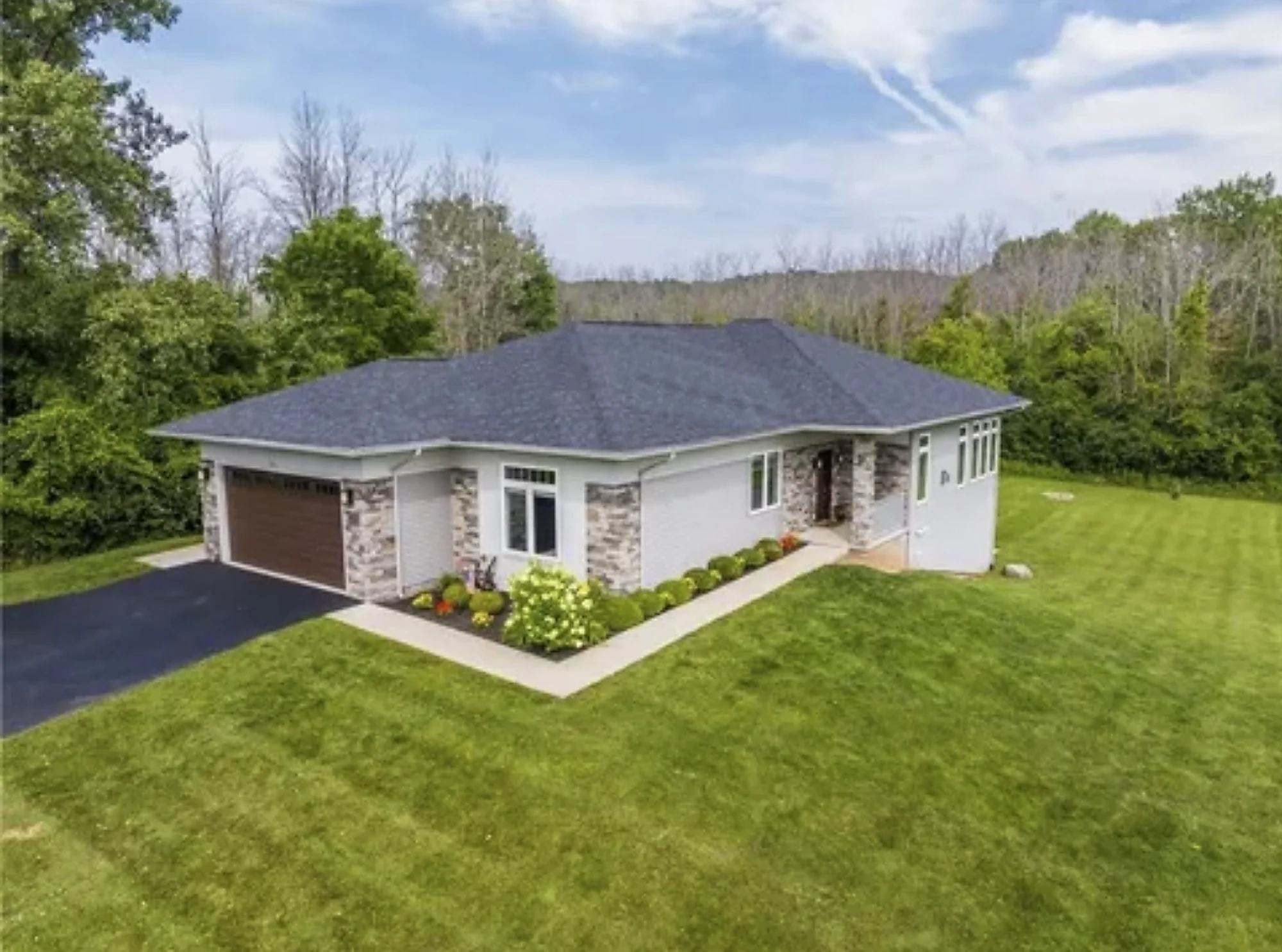 A single-story home with a dark hip roof, light gray siding, and stone accents around the garage and entry.